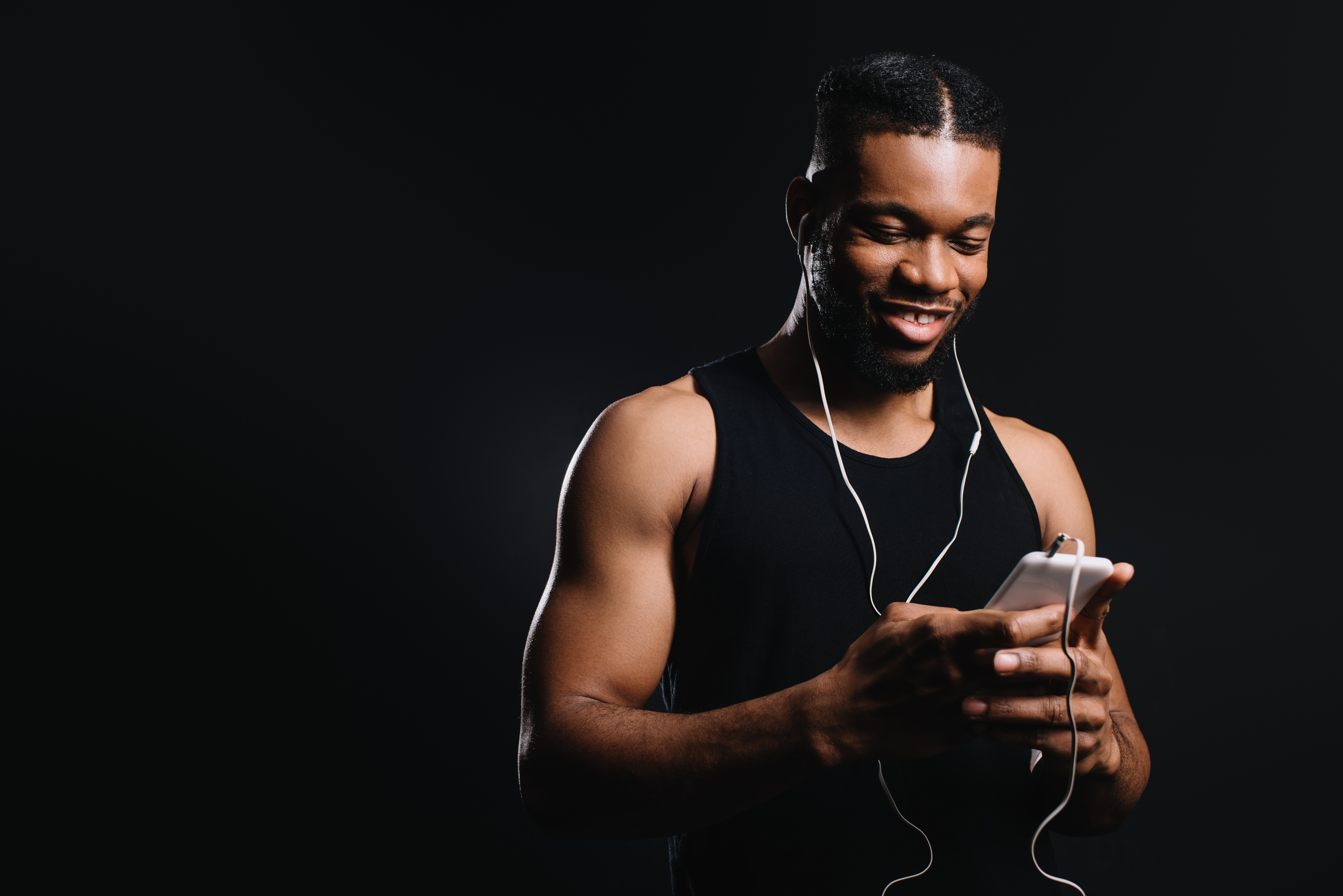 smiling muscular african american man in earphones using smartphone isolated on black